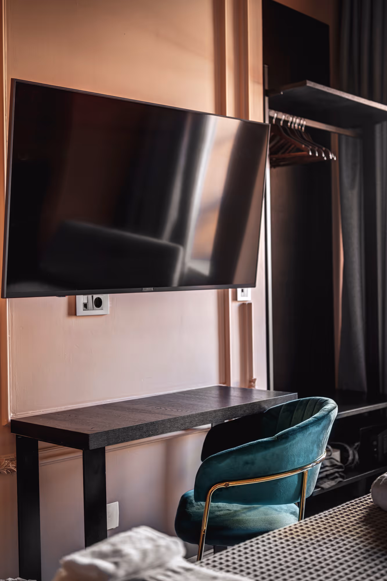 Modern room setup with a wall-mounted flat-screen TV above a dark wooden desk and a teal velvet chair with gold accents.