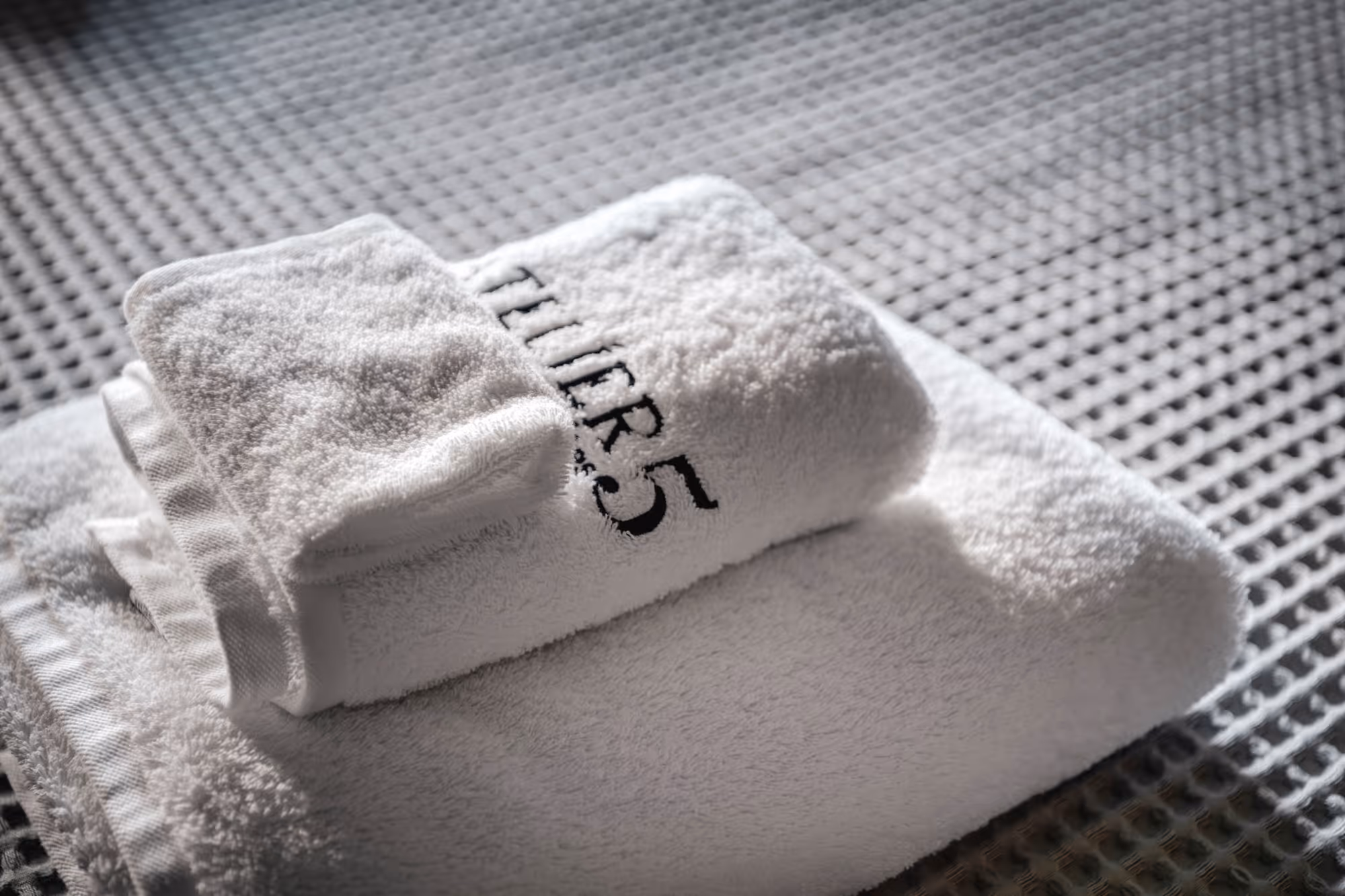 Stack of white towels on a textured surface, with one towel embroidered with 'THIR5'.