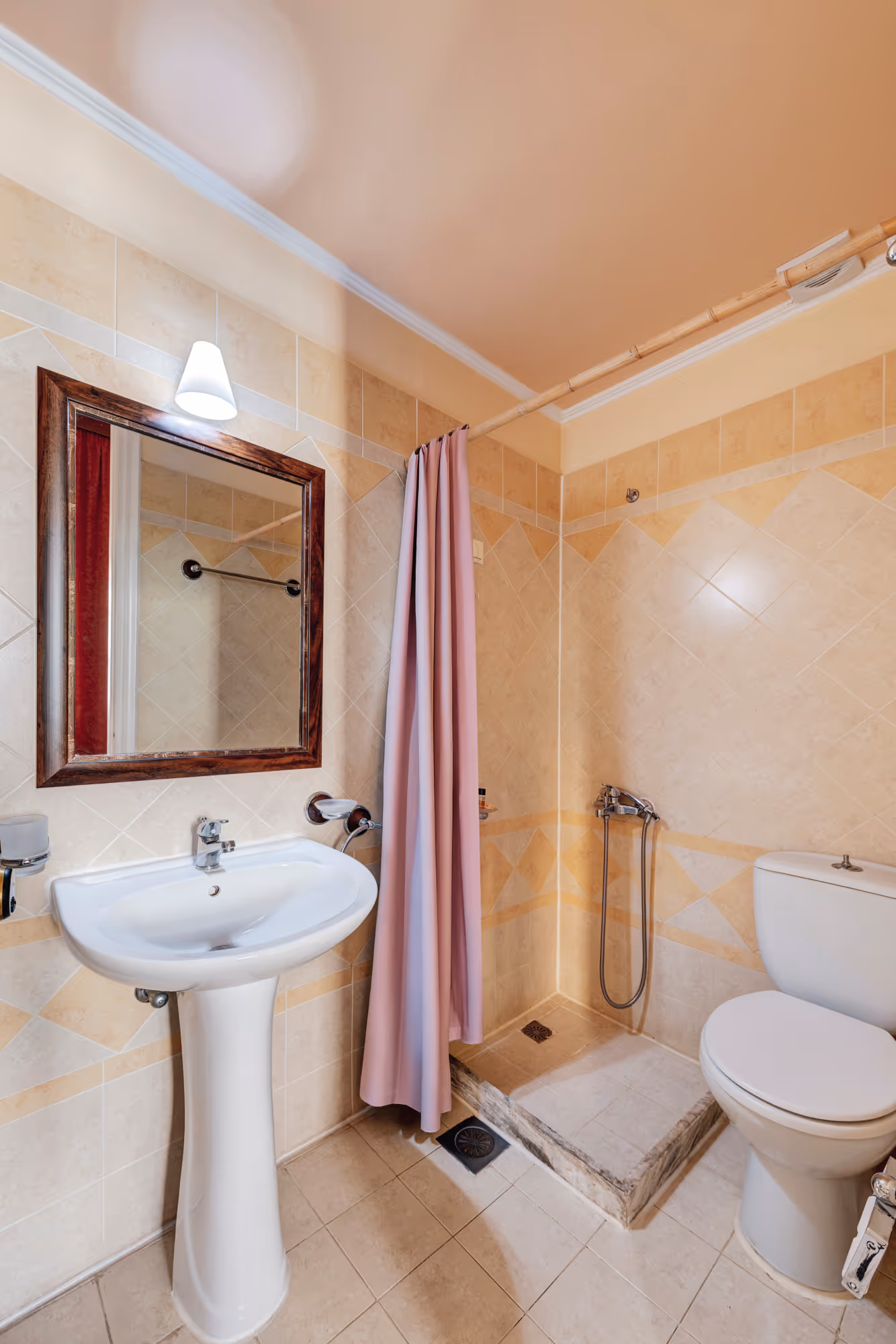 Compact bathroom with a white pedestal sink, framed mirror, pink shower curtain, and a white toilet.