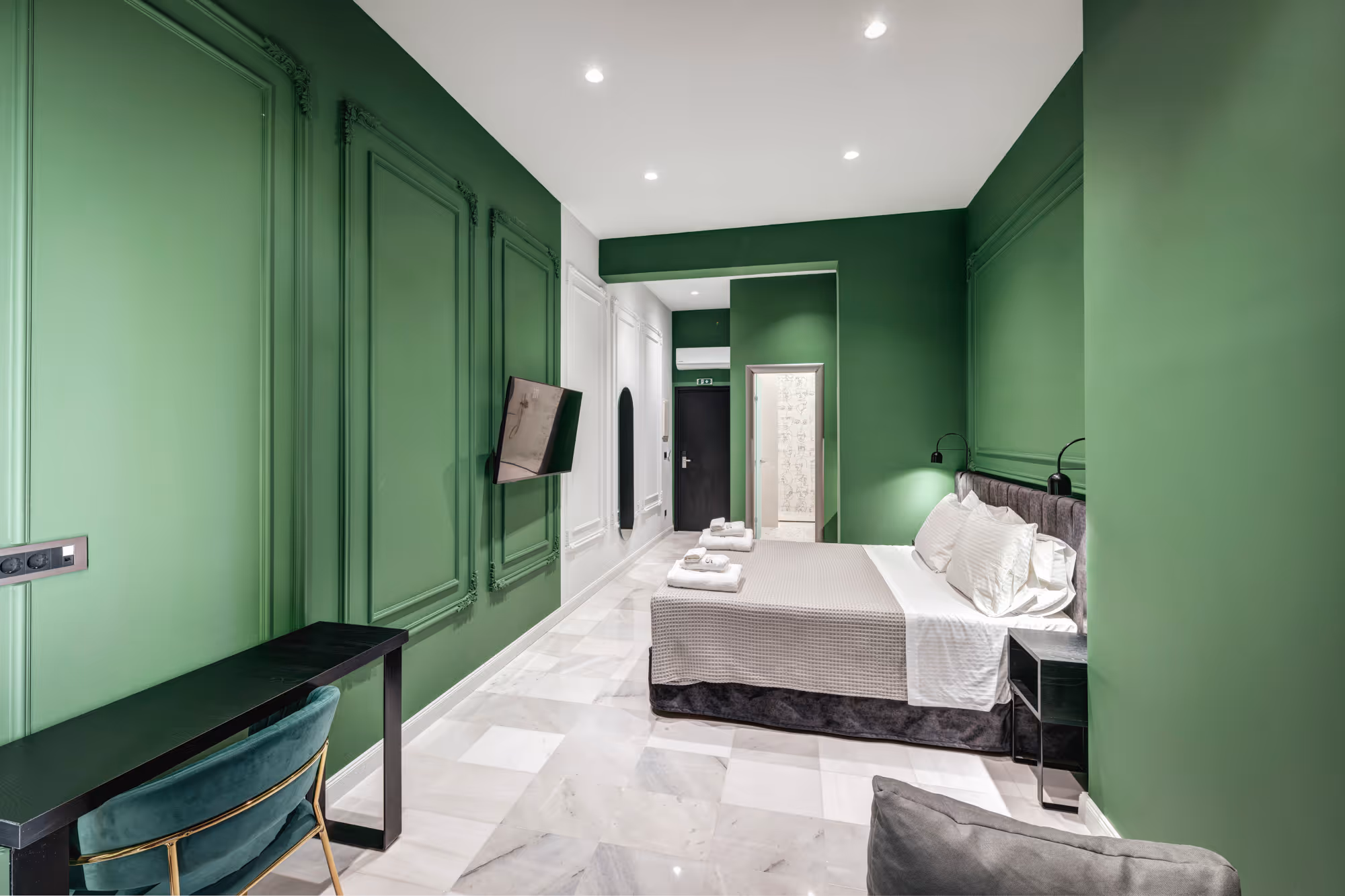 Modern hotel room with green walls, a double bed with light gray bedding, a black desk and chair, and marble floor tiles.