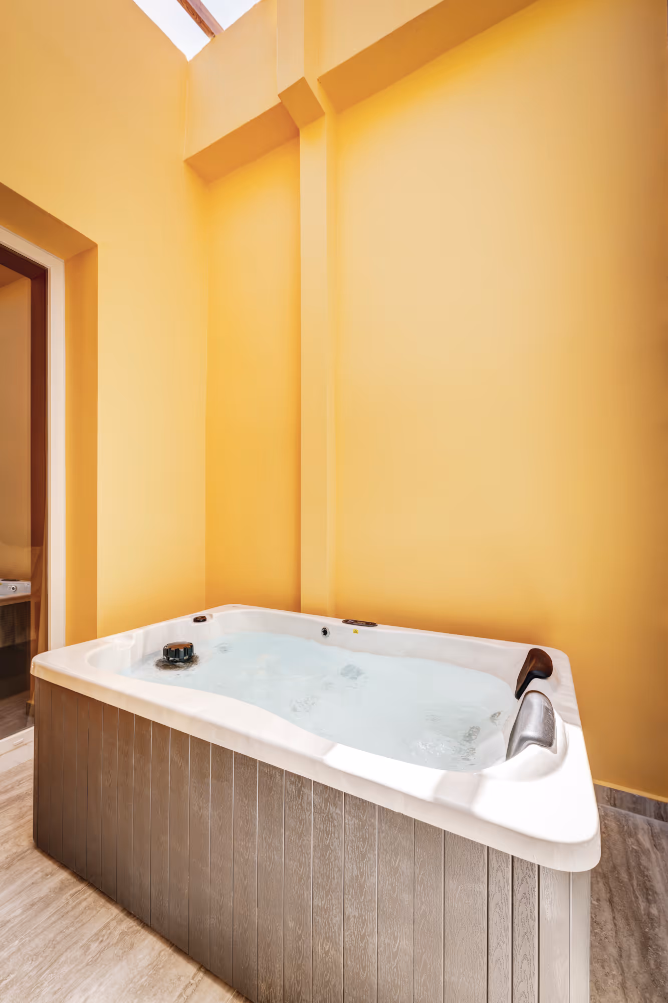 Indoor white jacuzzi tub with wooden paneling on the sides against yellow walls and a skylight above.