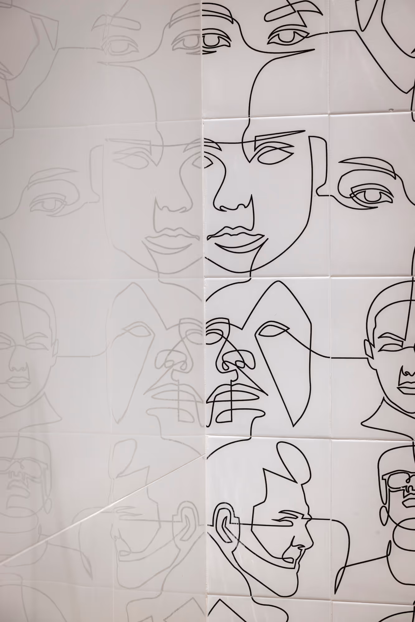 Wall tiles decorated with black continuous line art faces on a white background.