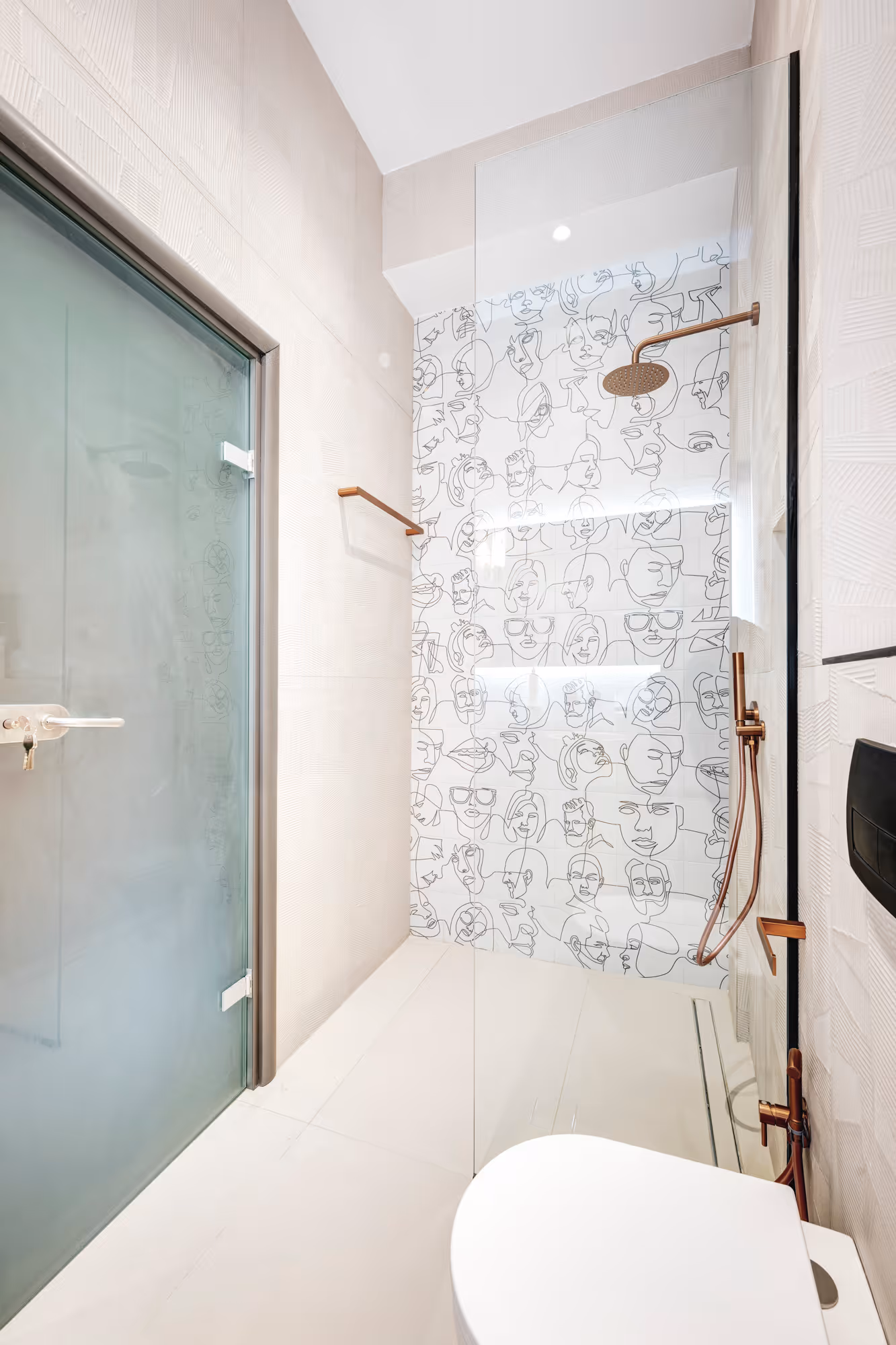 Modern bathroom with white toilet, glass shower enclosure featuring black line art face tiles and bronze shower fixtures.