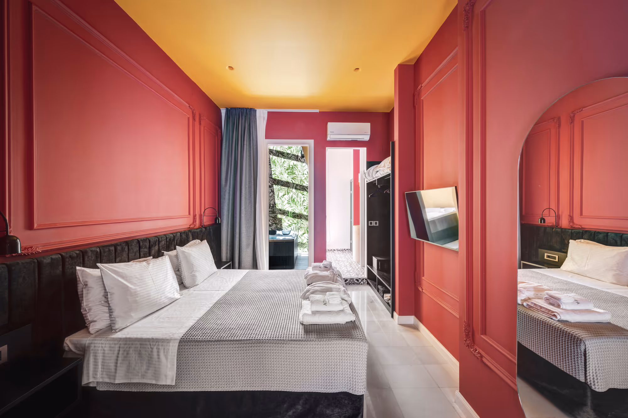 Modern hotel room with a large bed, white linens, red walls, yellow ceiling, and a wall-mounted TV.